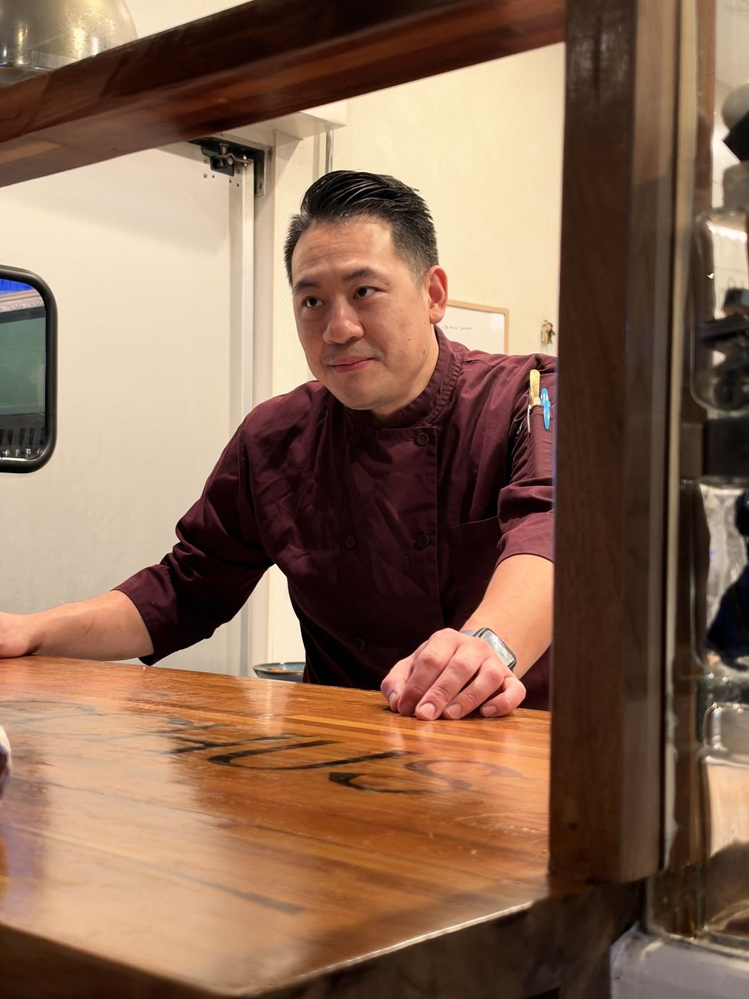 Executive Chef Danny Le leaning on the wooden pass of the Chez Bacchus kitchen