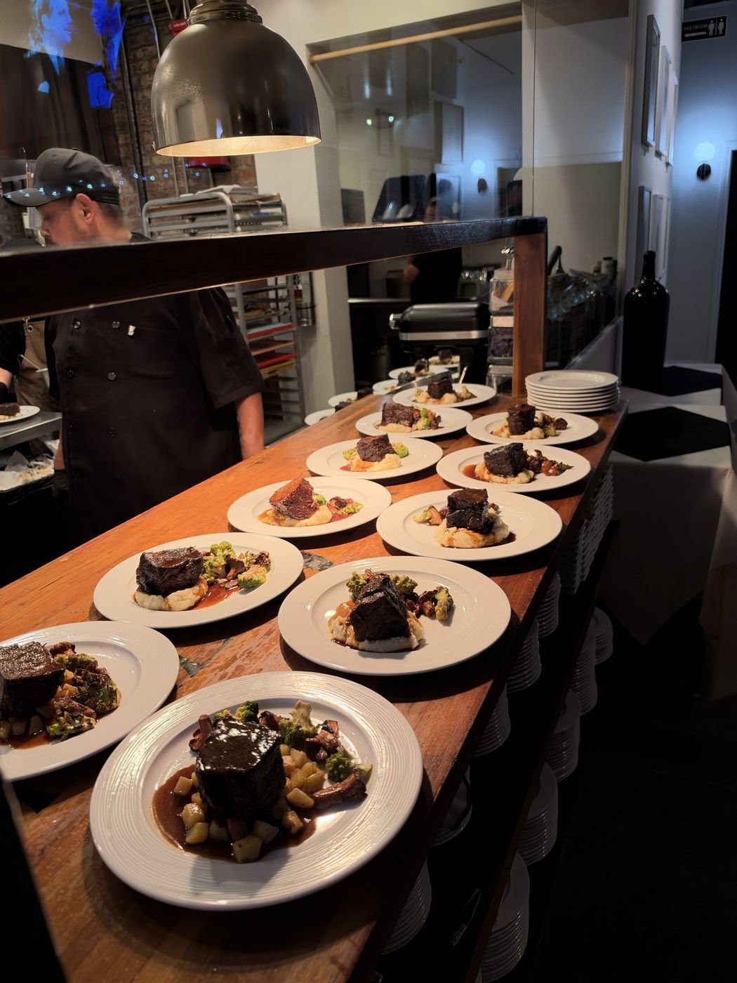 A row of plated main courses on the wooden pass, ready to go out to the dining room